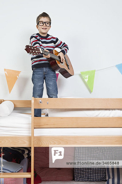 Ein Junge steht auf einem Etagenbett und spielt mit einer Gitarre.