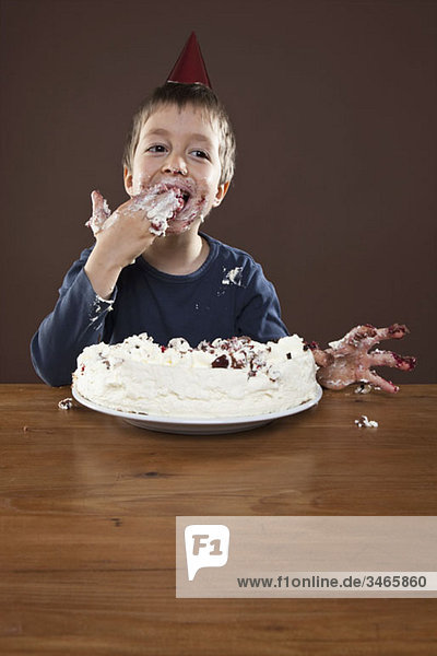 Ein Junge mit einem Partyhut  der Kuchen mit den Händen isst  Studioaufnahme