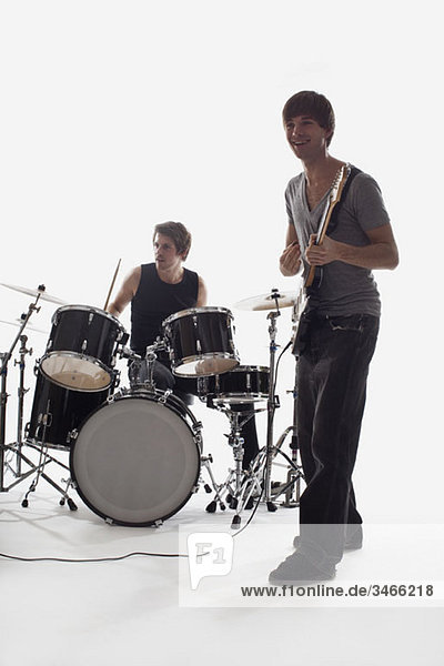 Ein Mann spielt E-Gitarre und ein Mann am Schlagzeug spielt  Studioaufnahme  weißer Hintergrund  hinterleuchtet