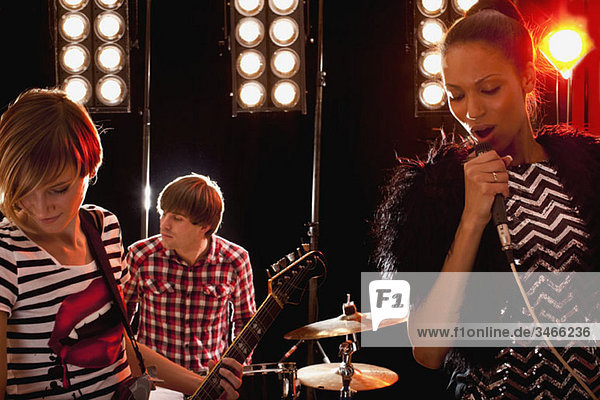 Eine Sängerin  begleitet von einem Mann am Schlagzeug und einer Frau an der Gitarre auf der Bühne.
