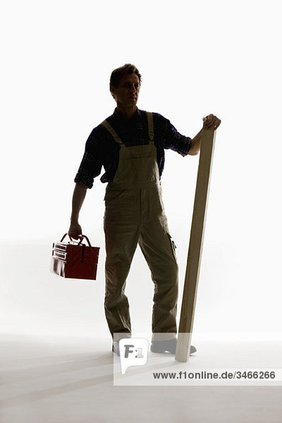 Ein Bauarbeiter  der einen Werkzeugkasten und ein Brett hält.