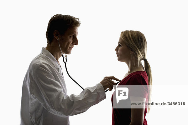 Ein Arzt  der mit einem Stethoskop eine Untersuchung an einem Patienten durchführt.