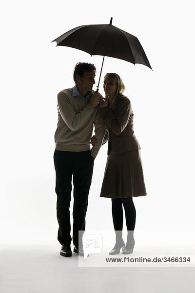Ein Mann und eine Frau kauern unter einem Regenschirm.
