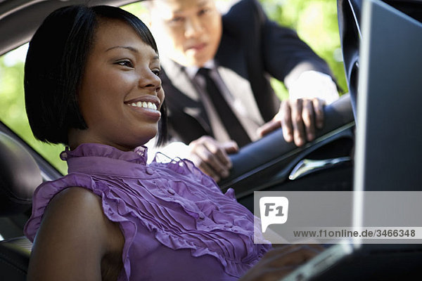 A woman sitting in a car using a laptop while a man leans into the car