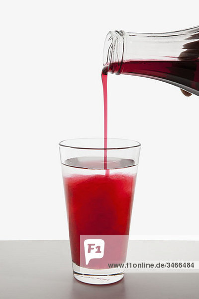 Detail eines Fruchtsirups  der in ein Glas Wasser gegossen wird.