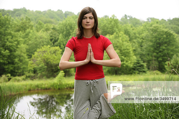Woman practising yoga by a pond  front view