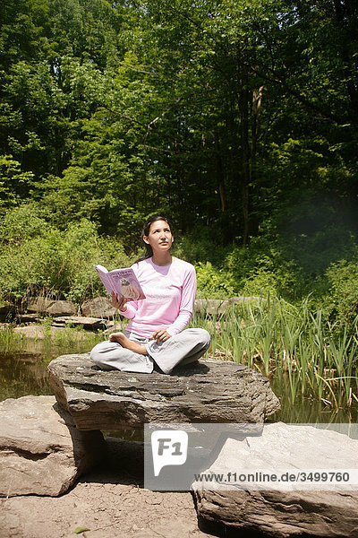Frau sitzt mit Buch auf einem Stein