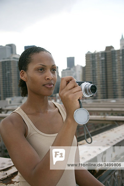 Woman standing on the Brooklyn Bridge and holding a digital camera  skyline of New York in the background  USA