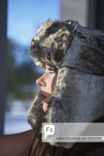 Woman wearing fur hat looking through window