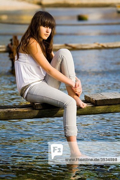 Teenager girl is sitting on an old rotten pier