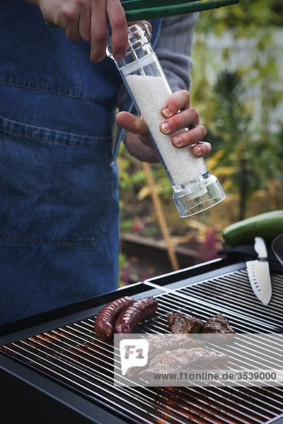 Person adding salt on meat cooked on barbecue grill
