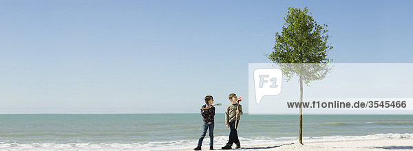 Kinder stehen mit Gartengeräten neben einem Baum  der am Strand gepflanzt wurde.