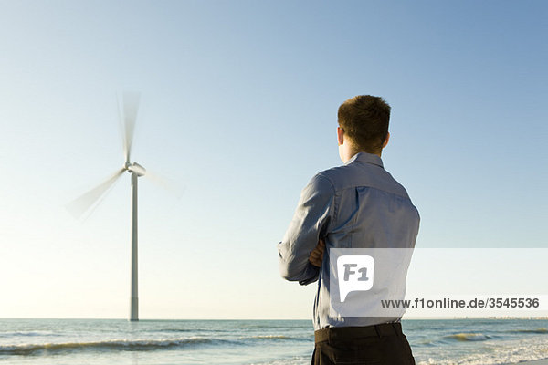 Mann am Strand beobachtet Offshore-Windkraftanlage bei der Arbeit