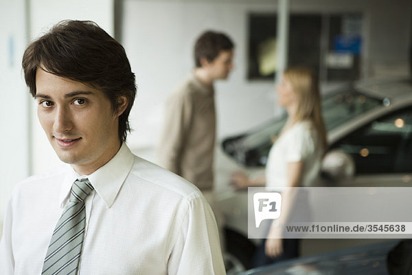 Car salesman in dealership showroom  potential buyers in background