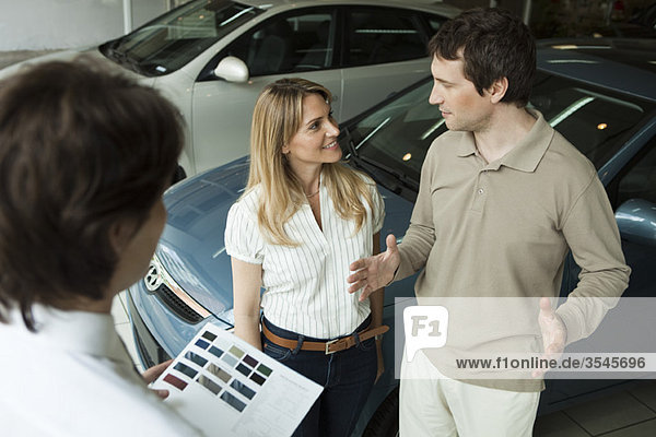 Paar im Autohaus-Showroom diskutiert mit Verkäufer über neue Fahrzeugoptionen