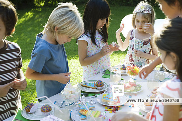 Kinder wählen Süßigkeiten vom Tisch bei der Geburtstagsfeier im Freien aus
