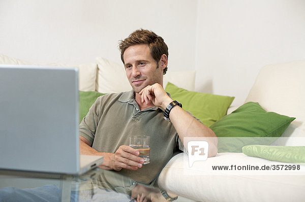 Zufriedener Mann im Wohnzimmer schaut auf Laptop