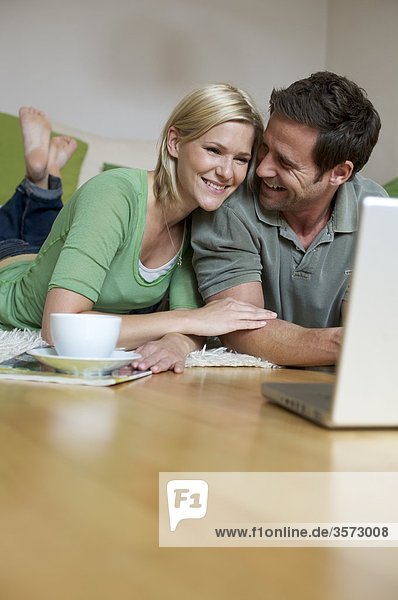 Couple lying on floor and looking at laptop