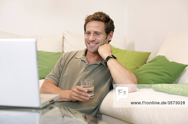 Fröhlicher Mann im Wohnzimmer schaut auf Laptop