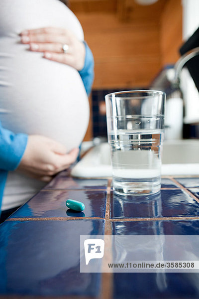 Schwangere mit Wasser und Vitaminpillen