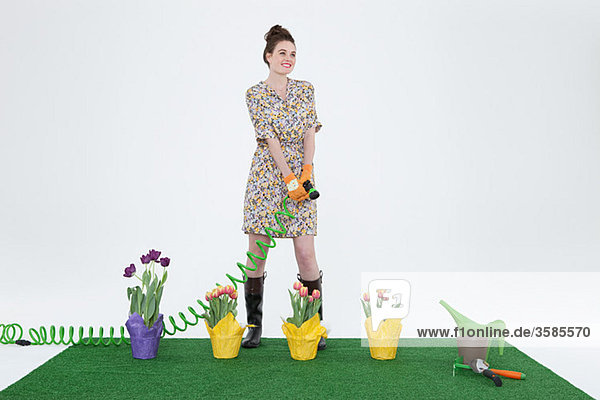 Frau mit Schlauch und Blumen auf Kunstrasen