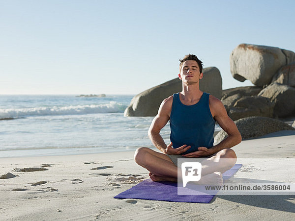 Young man doing yoga on beach