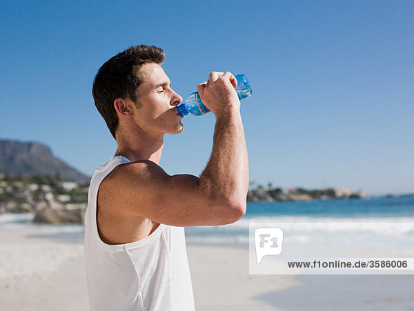 Junger Mann trinkt Wasser am Strand