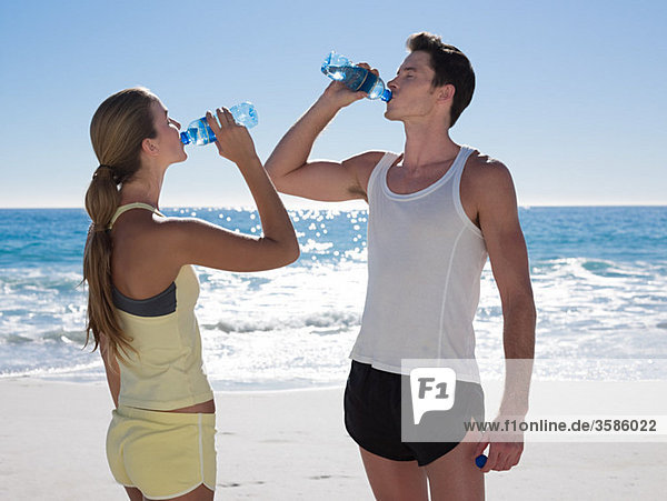 Young couple with bottles of water on beach