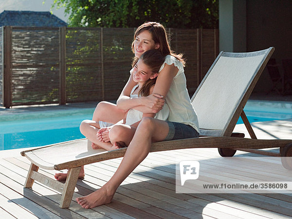 Girl and mother on lounge chair by swimming pool