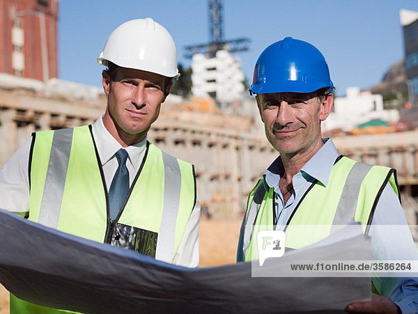 Mature men with blueprint on construction site