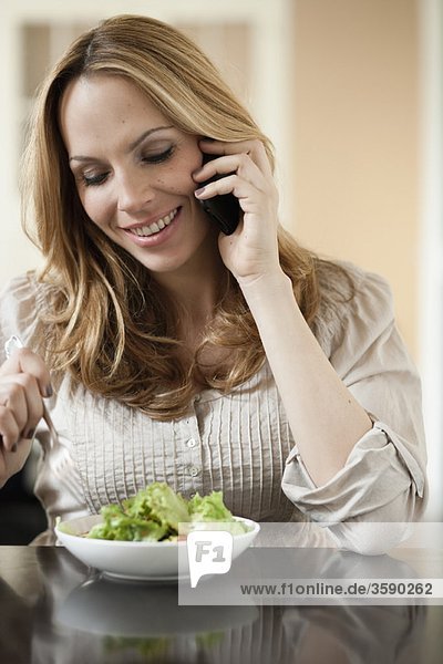 Frau auf dem Handy isst Salat