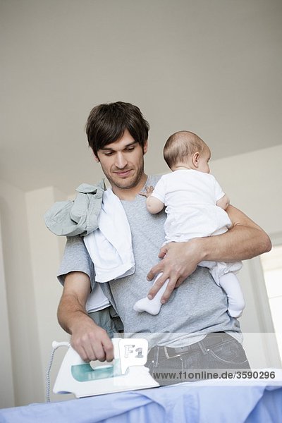 Father with baby in arm ironing