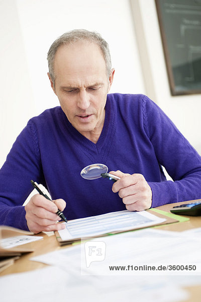Man looking through a magnifying glass while filling his tax form