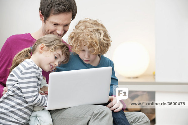 Nahaufnahme eines Mannes  der seinem Sohn und seiner Tochter bei der Benutzung eines Laptops hilft.