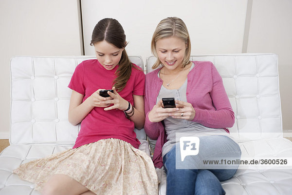 Woman with her daughter text messaging on mobile phones