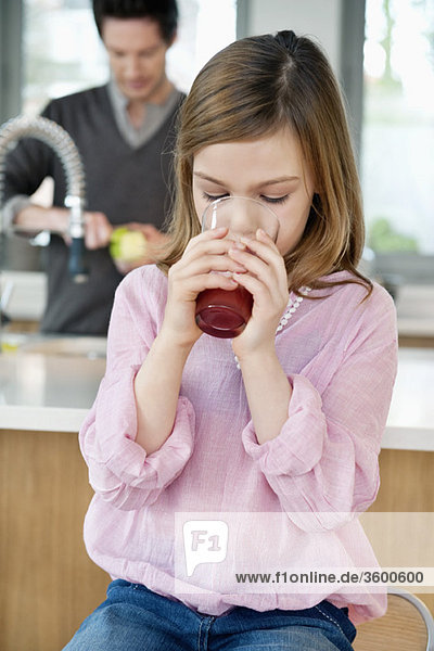 Girl drinking juice with her father standing behind her