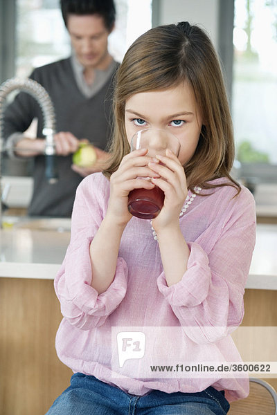 Girl drinking juice with her father standing behind her