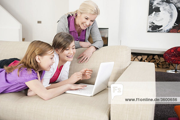 Two girls using a laptop on a couch with their grandmother standing beside them