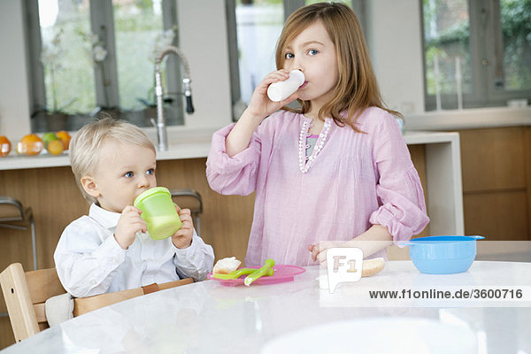 Mädchen trinkt Milch mit ihrem Bruder am Frühstückstisch.