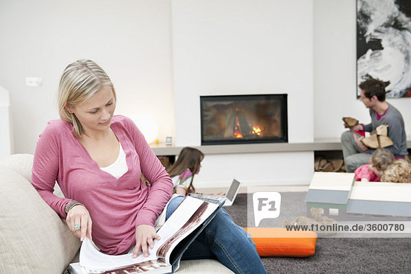 Frau beim Lesen einer Zeitschrift mit ihrer Familie im Wohnzimmer