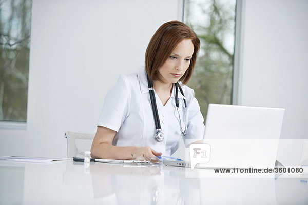 Female doctor sitting in an office inserting CD into a laptop