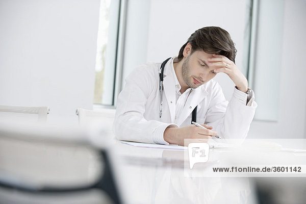 Ein männlicher Arzt sitzt in seinem Büro und sieht verärgert aus.