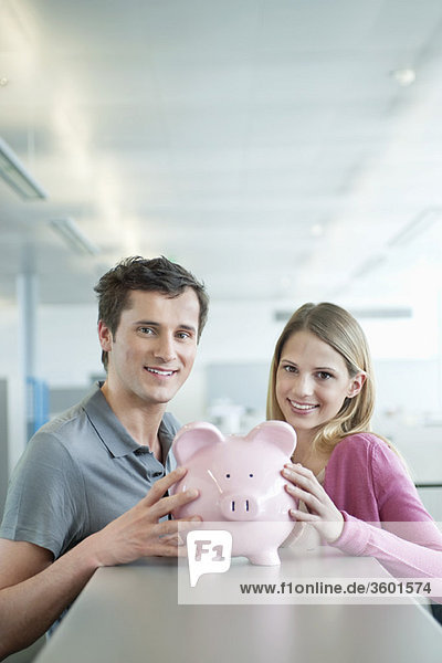 Geschäftsleute  die ein Sparschwein halten und lächeln