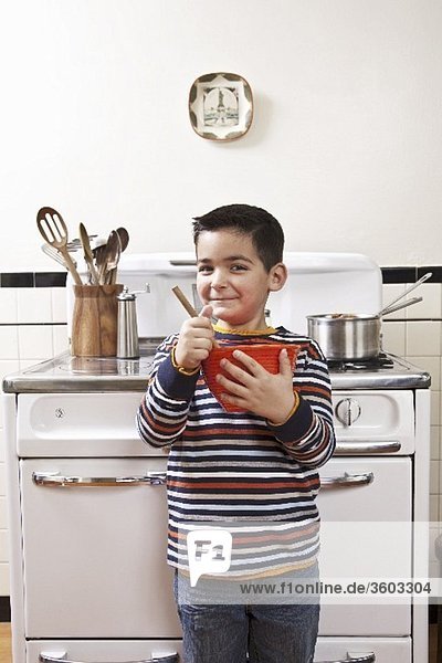 Kleiner Junge mit Rührschüssel vor dem Küchenherd