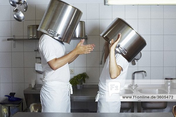 Two chefs having discussion with large pans on their heads