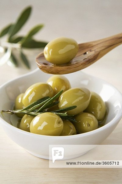 Grüne Oliven im Schälchen und auf Holzlöffel