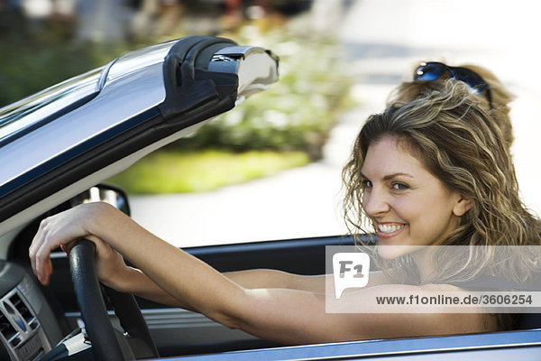Young woman out with friend for pleasure drive in convertible