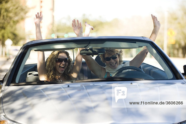 Friends riding in convertible with arms raised in the air