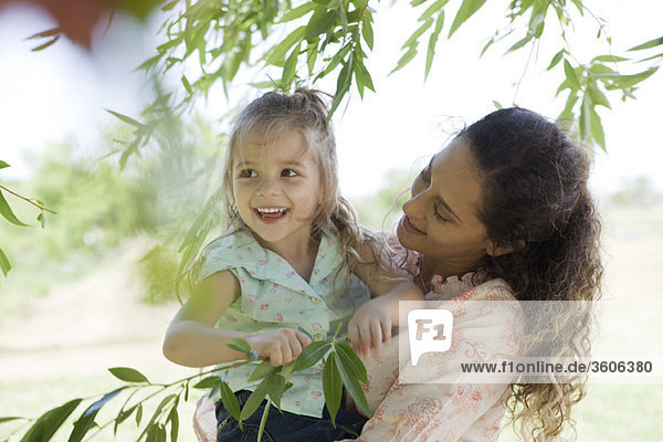 Mutter hält junge Tochter im Freien  Mädchen hält sich an Baumästen fest
