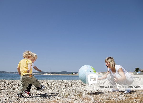 Mutter mit Zwillingen am Strand beim Ballspielen